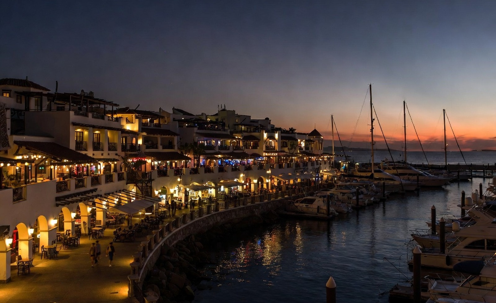 A harbor promenade at dusk with lights reflecting on the water.